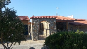 A stone building with a red-tiled roof, a stone archway, and a metal antenna. - Creta Suites (Ierapetra)