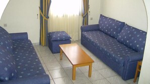 A compact living space with a sofa set, a small table, and curtains. - Creta Suites (Ierapetra)