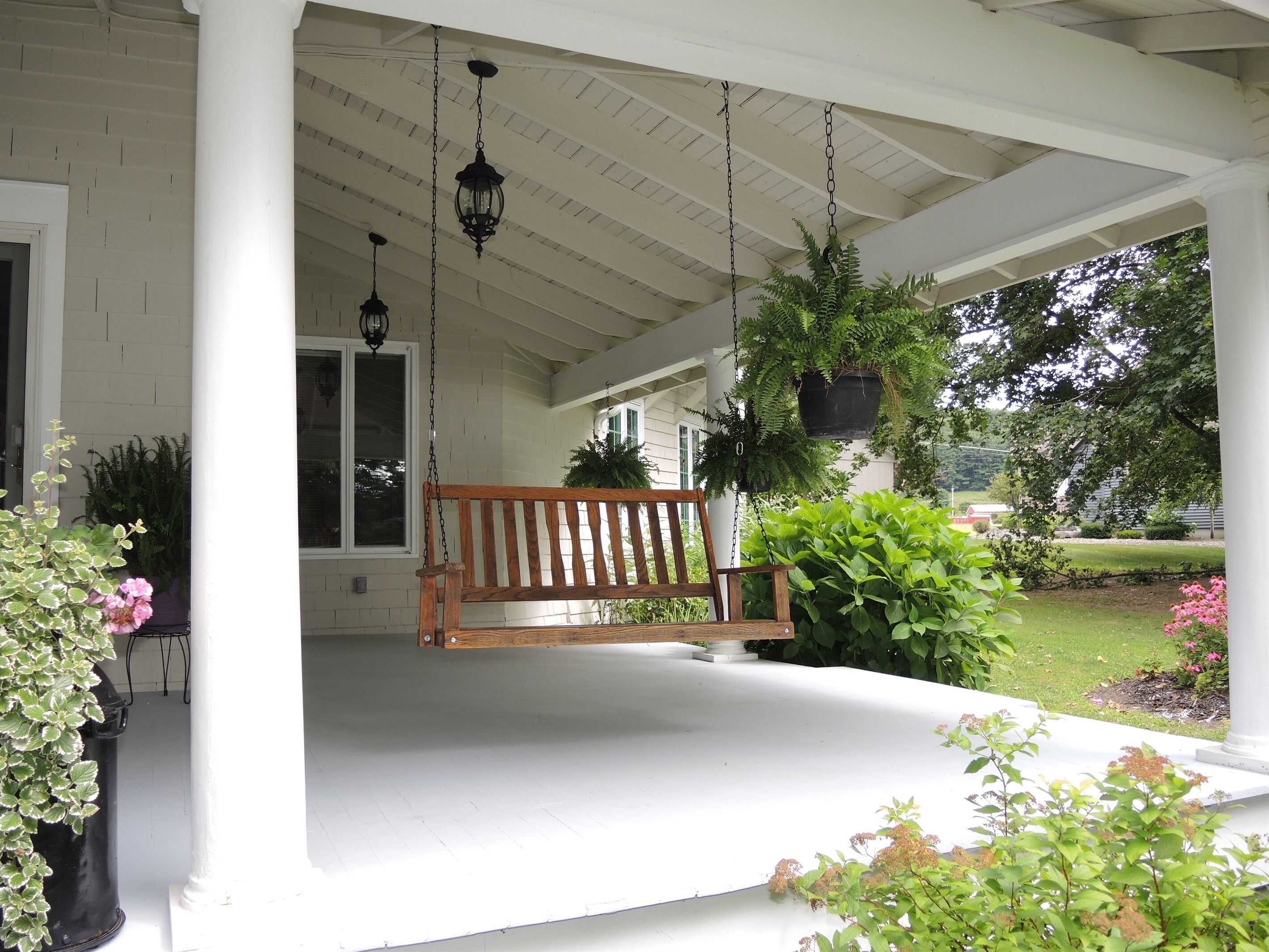 A porch with a wooden bench, hanging lanterns, and potted plants.