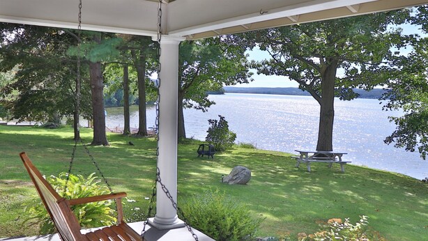 Eine Veranda mit einer Schaukel, mit Blick auf einen See, Bäume und einen Picknicktisch.
