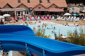 A pool area with a blue slide, lounge chairs, and a building with a tiled roof in the background. - Mobile home for 4 people, 2 bedrooms, 300 m from the beach (Saint-Brevin-les-Pins)