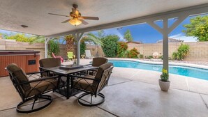 An outdoor patio with a pool, a ceiling fan, and a table with chairs.