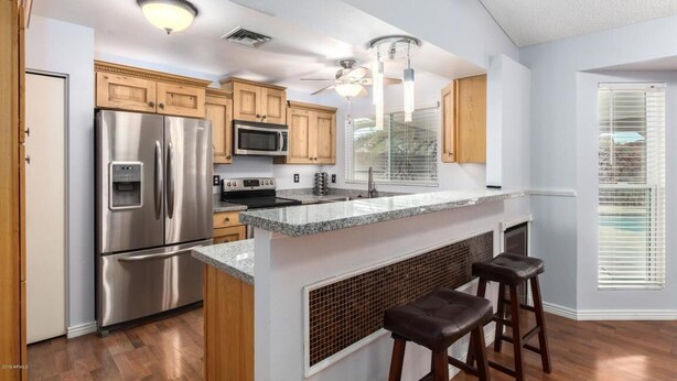 A modern kitchen with stainless steel appliances, wooden cabinets, and a bar area with stools.