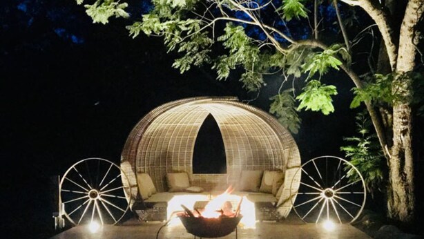 A dome-shaped outdoor seating area with a fire pit in the center, surrounded by two large wheels and a tree.