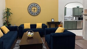 Un soggiorno con due divani blu, una parete gialla e un orologio.