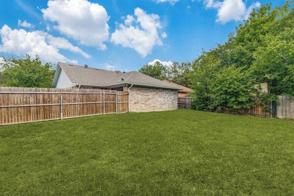 A backyard with a stone house, a wooden fence, and a well-maintained lawn. - Beautiful 3 bedrooms & 2 full bath in McKinney, just minute away from McKinney Historic Downtown. (McKinney)