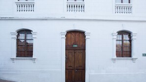 A white building with a large wooden double door and two windows with wooden frames. - COZY & BRIGHT APT - 5 min to Old Town (Quito)