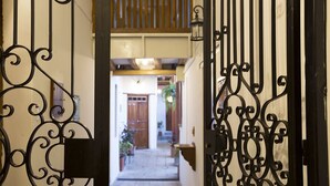An ornate wrought iron gate leading to a narrow corridor with a wooden ceiling and a view of a door and plants in the distance. - COZY & BRIGHT APT - 5 min to Old Town (Quito)