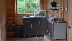 Een kleine keuken met een raam, een spoelbak, kastjes, een koelkast en een kleine prullenbak.