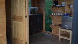 Een houten hutje van binnen, met een kitchenette, een kleine tafel en een koelkast.