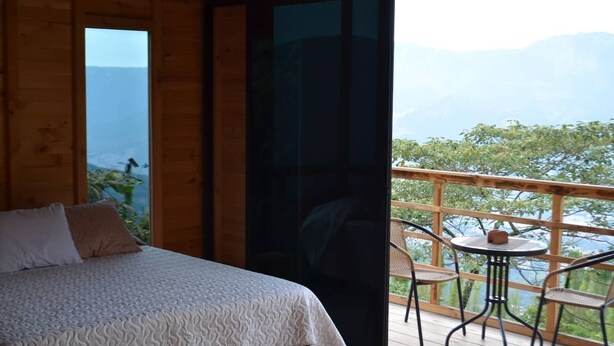 Een slaapkamer met een bed, een balkon met een tafel en stoelen, en uitzicht op zee en bergen.