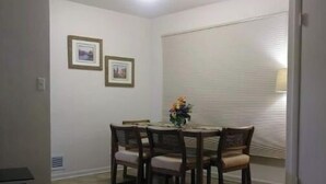 A dining area with a round table and four chairs, a small side table, and a window with blinds.