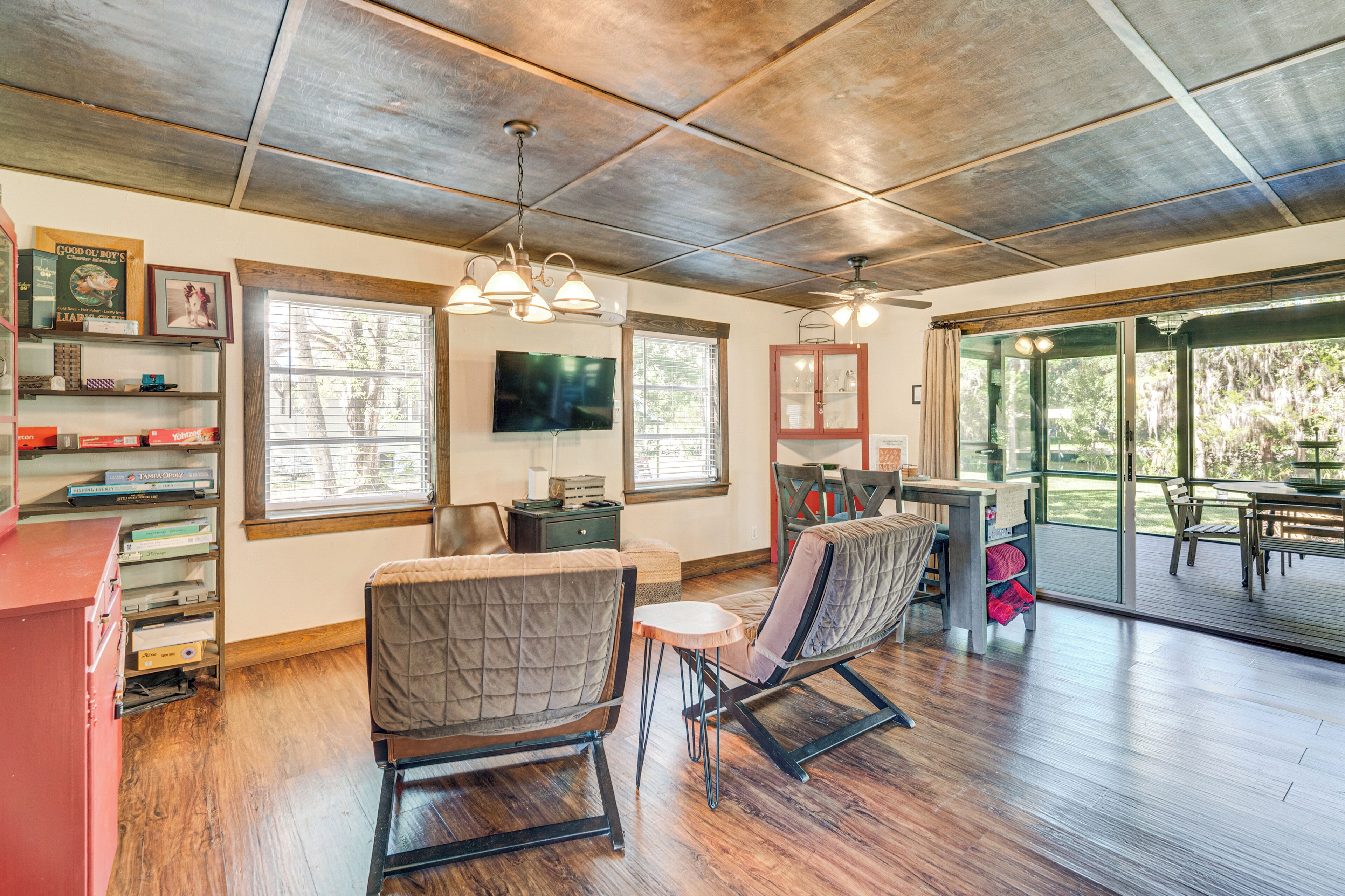 A spacious living area with a wooden ceiling, a television mounted on the wall, and a large window providing a view of the outdoors.