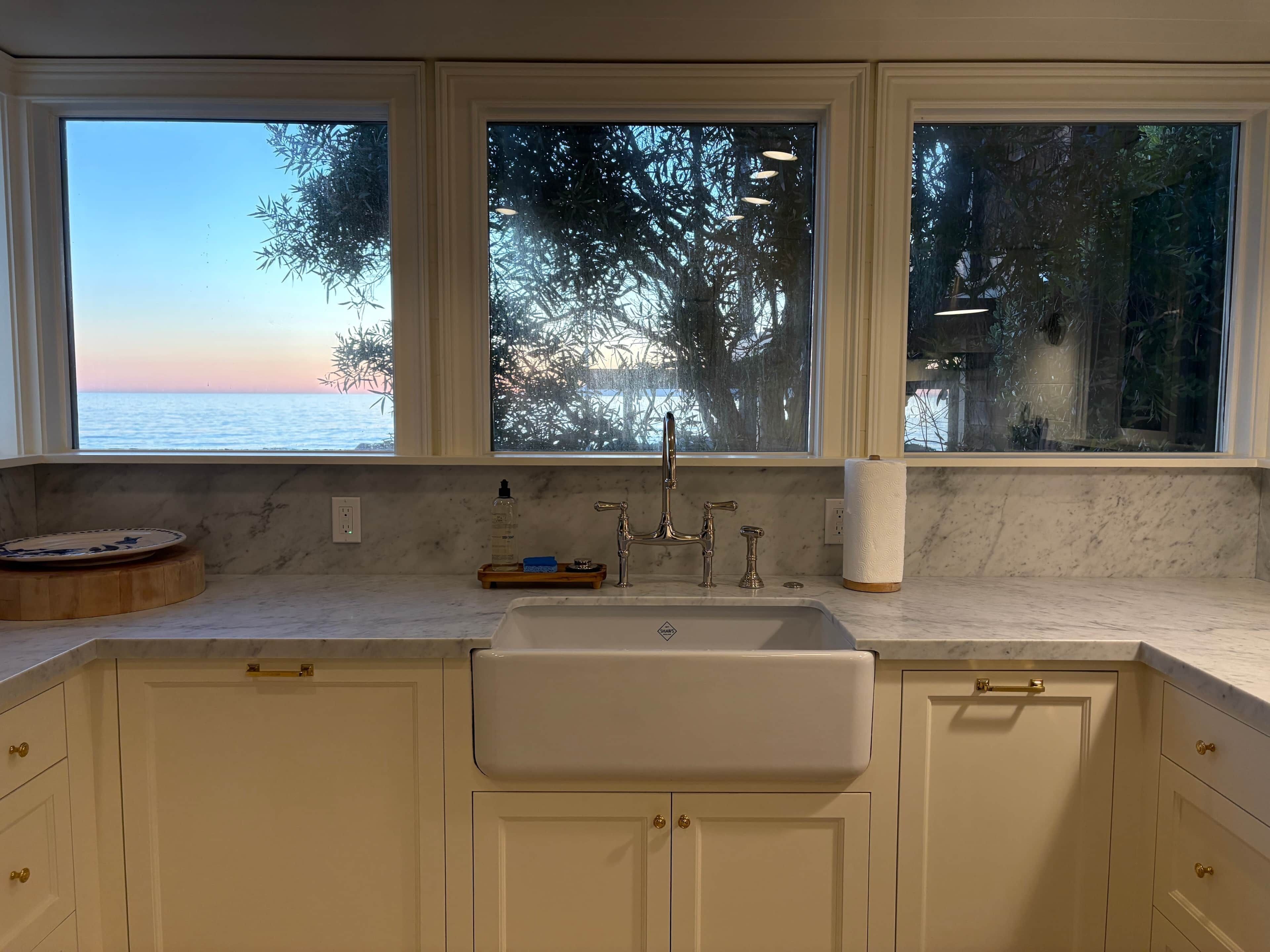 A kitchen with a sink, three windows, and a view of the sea.