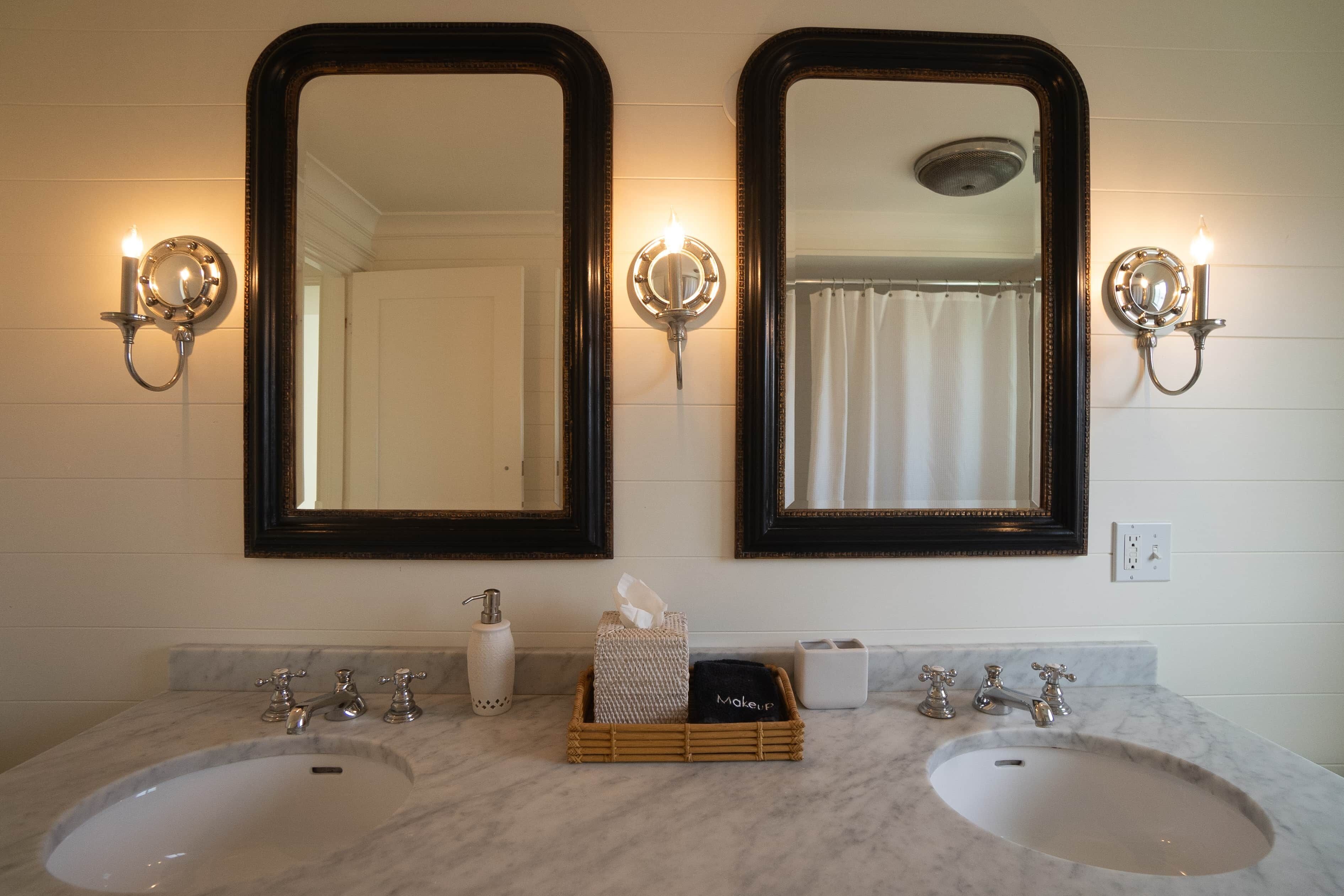 A bathroom with two sinks, mirrors, wall sconces, and a tissue box.