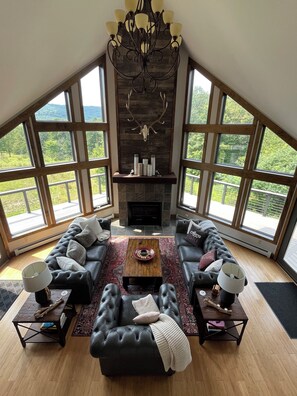 A spacious living room with a fireplace, large windows, and a high ceiling. - Crazy spacious hillside ski chalet! WOW-views and expansive wraparound deck! (Great Valley)