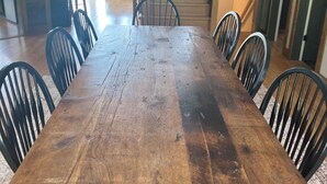 Un comedor amplio con una larga mesa de madera y sillas negras, una araña con ramificaciones similares a astas, y vistas al exterior a través de grandes ventanales.