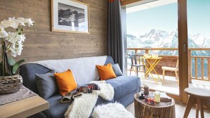 A living room with a sofa, a framed picture, and a view of mountains through a balcony door.