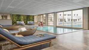 A modern indoor pool area with lounge chairs, a wooden boat, and a view of the outside buildings.