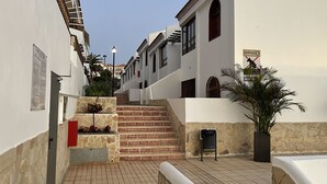 Une rue étroite bordée de bâtiments blancs, un escalier en pierre et un pot de fleurs.