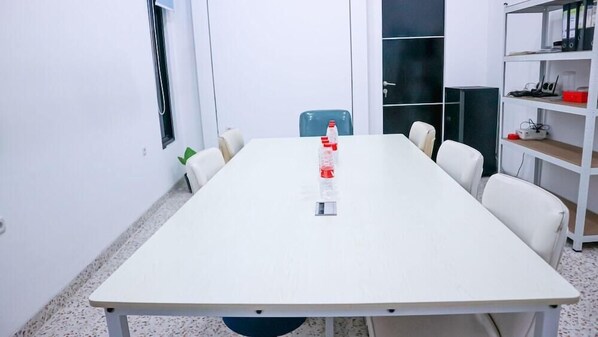 A conference room with a long table, chairs, a water bottle, and a shelf with binders. - Super OYO 3728 Tunas Plaza Residence (Bekasi)