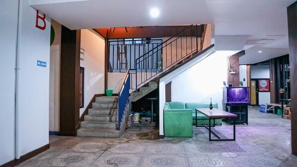 A lobby with a staircase, a green sofa, a small table, and a television. - Super OYO 3728 Tunas Plaza Residence (Bekasi)
