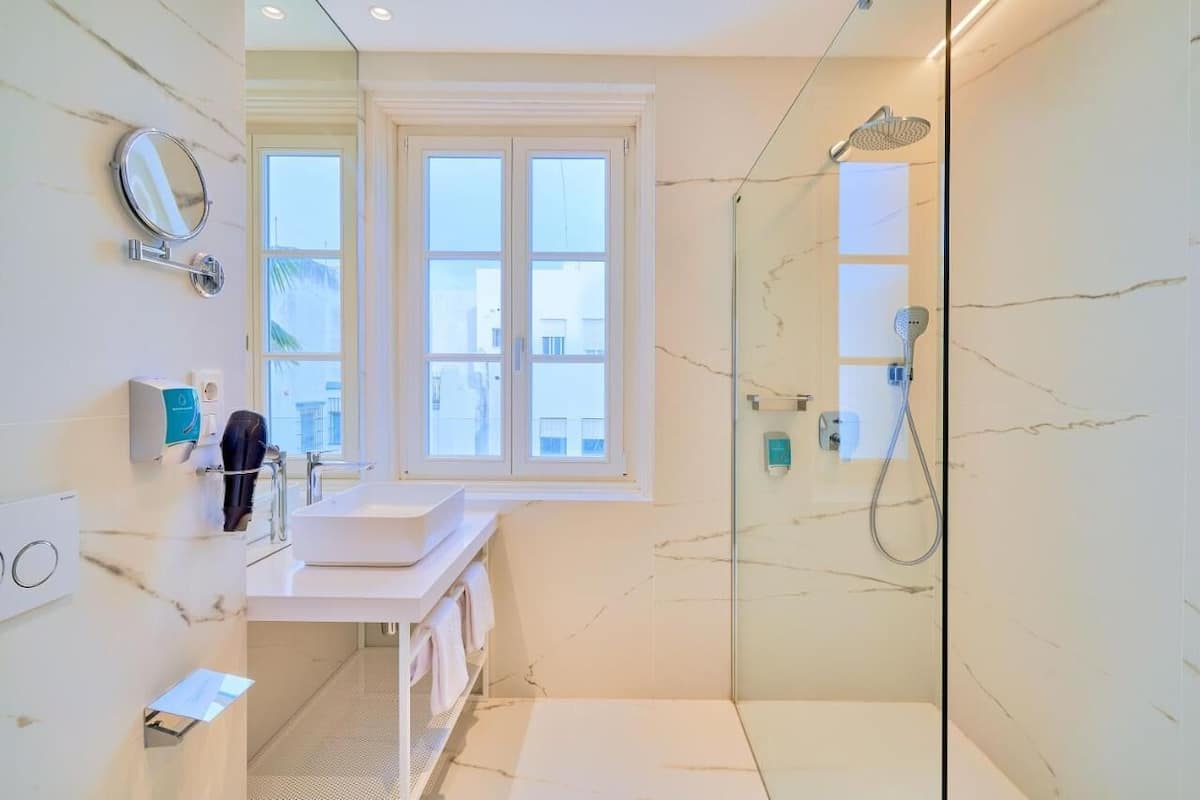 A modern bathroom with a large window, a glass-enclosed shower, and a marble-tiled floor.