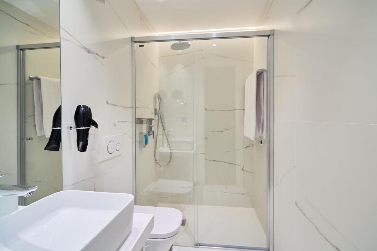 A modern bathroom with a glass-enclosed shower, a white bathtub, and a toilet.