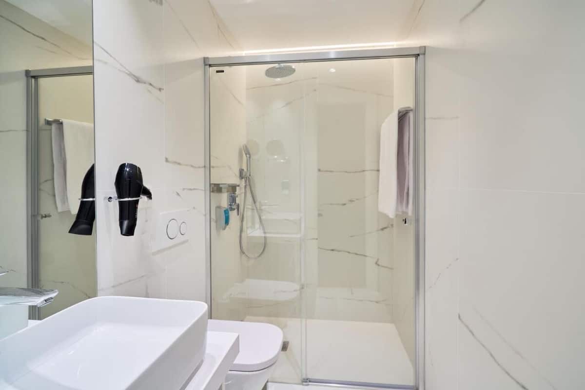 A modern bathroom with a glass-enclosed shower, a white bathtub, and a toilet.