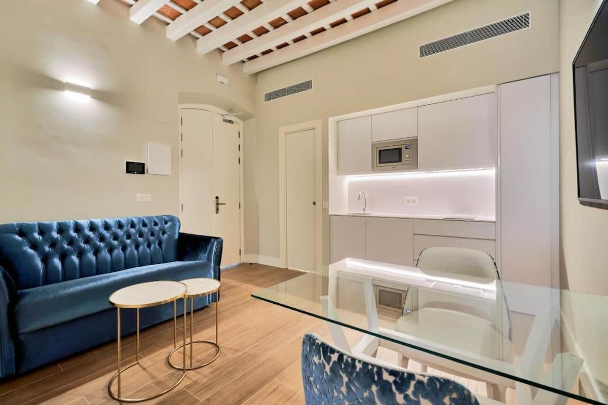A modern living room with a blue sofa, a glass coffee table, and a white dining table.
