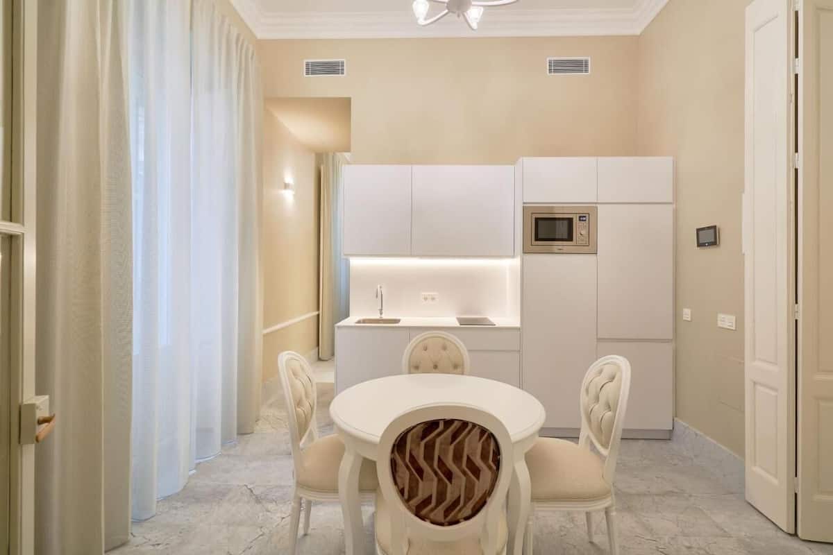 A modern kitchen with white cabinetry, a built-in microwave, and a round dining table with upholstered chairs.
