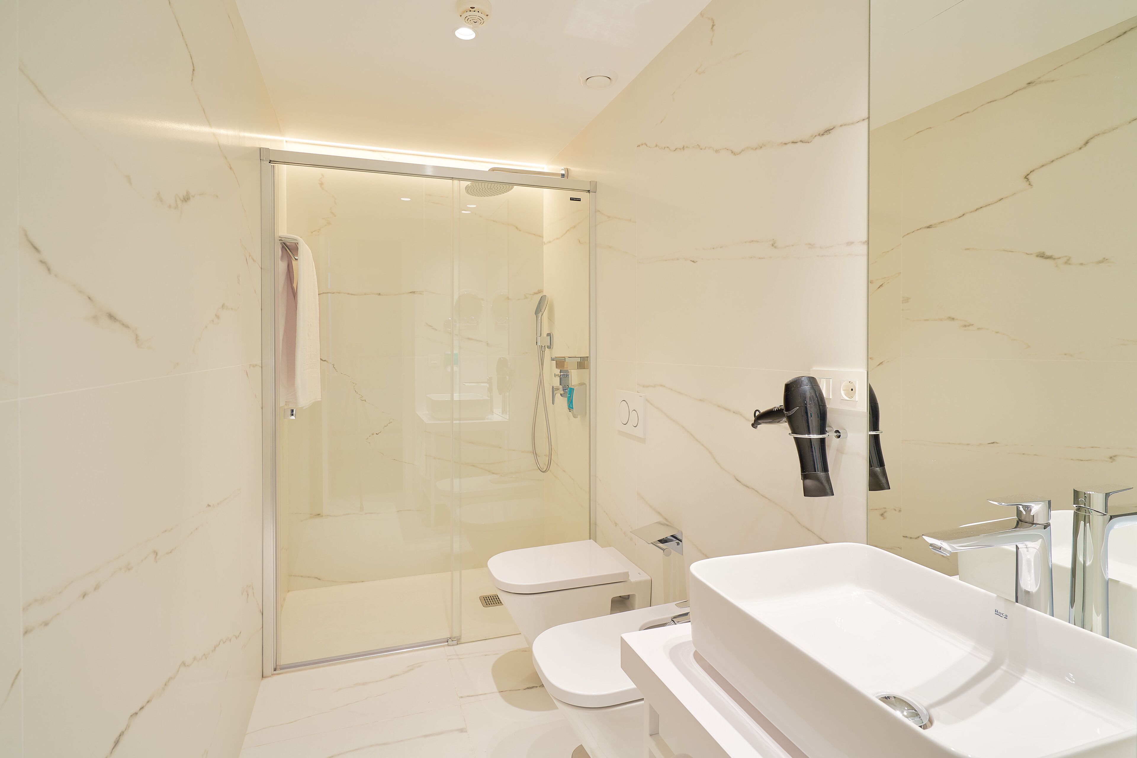A modern bathroom with a glass-enclosed shower, a white toilet, and a large sink with a mirror.