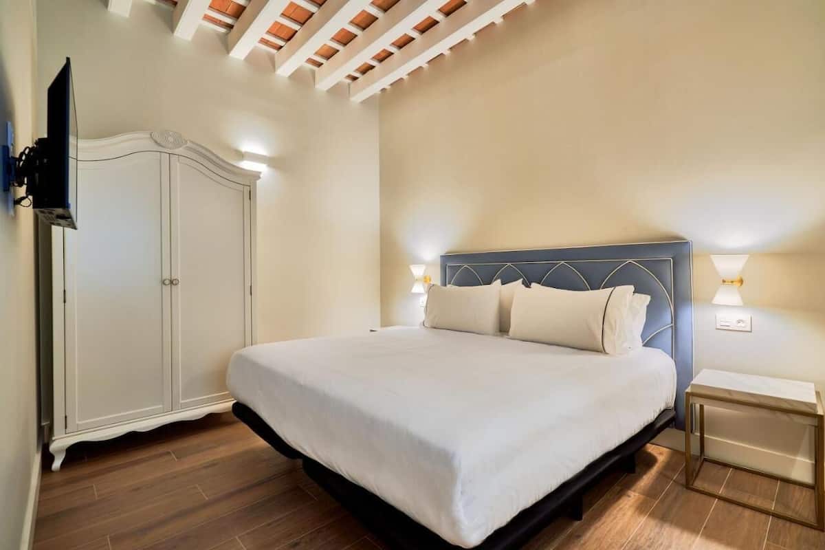A bedroom with a bed, a wardrobe, a TV, and a nightstand with a lamp.