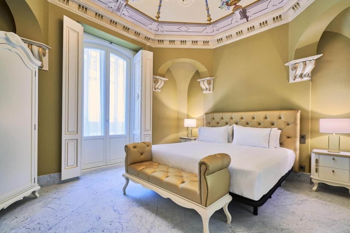 A luxurious bedroom with a large bed, a chaise lounge, and a classic chandelier.