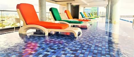 A poolside area with lounge chairs and a tiled floor.