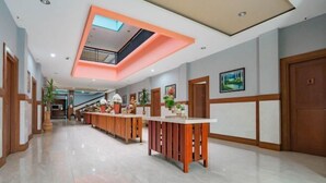 A hotel lobby with a central reception desk, a staircase, and a ceiling with recessed lighting.
