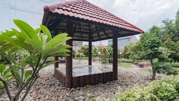A gazebo with a tiled roof, surrounded by gravel and greenery.