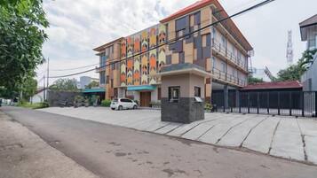 Un edificio de varios pisos con fachada colorida, entrada protegida por un portón y un estacionamiento con automóviles.
