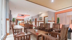 A spacious dining area with wooden furniture and a long table, surrounded by walls with framed pictures and a decorative orange panel.