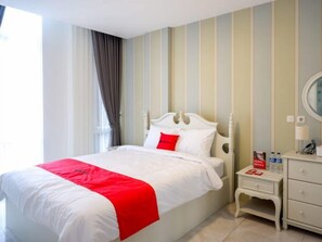 A hotel room with a bed, a bedside table, a nightstand, a mirror, and a window with curtains. - Reddoorz Plus @ Madukoro Raya Semarang (Semarang)