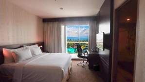 A hotel room with a bed, a desk, a chair, a television, and a large window with a view of a pool and landscape. - Labersa Toba Hotel and Convention Centre Balige (Balige)