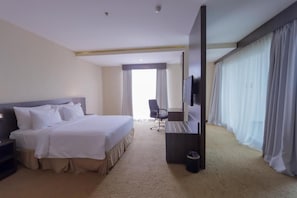Habitación de hotel con una cama, un escritorio, una silla, un televisor y cortinas.