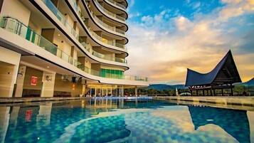 Ein modernes Hotel mit geschwungener Fassade, einem Schwimmbad und Blick auf die Berge.