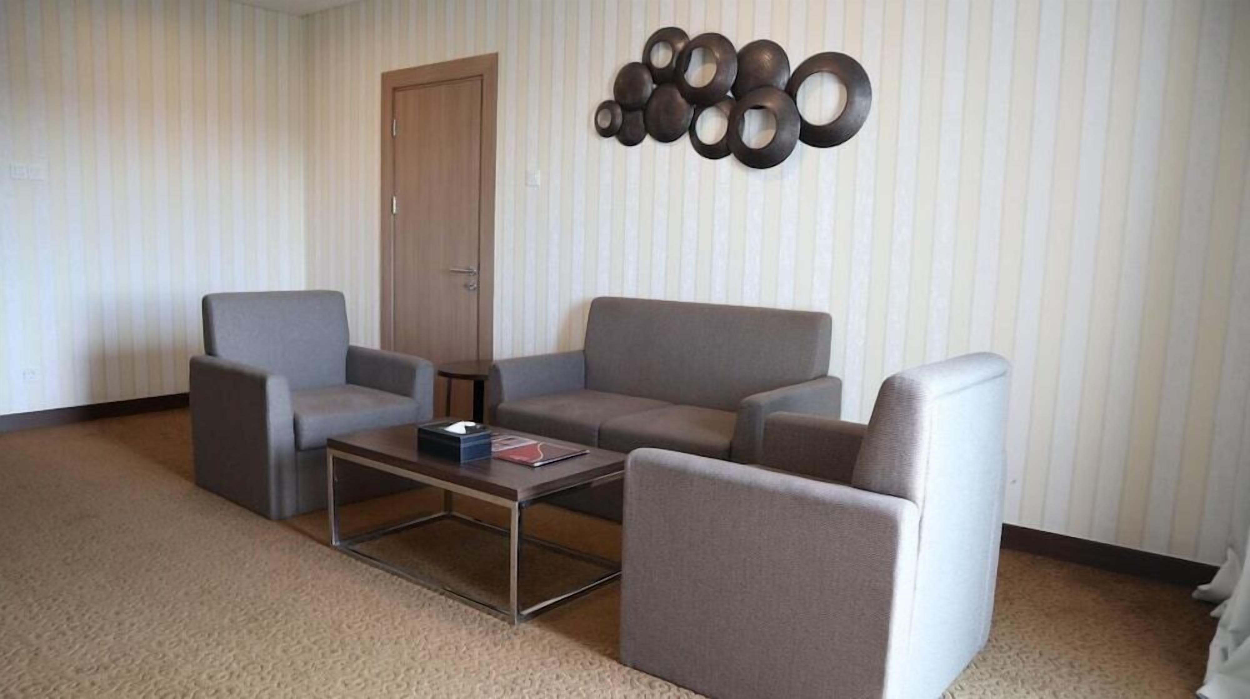 A living room with a sofa, two armchairs, a coffee table, and a wall-mounted decorative piece.