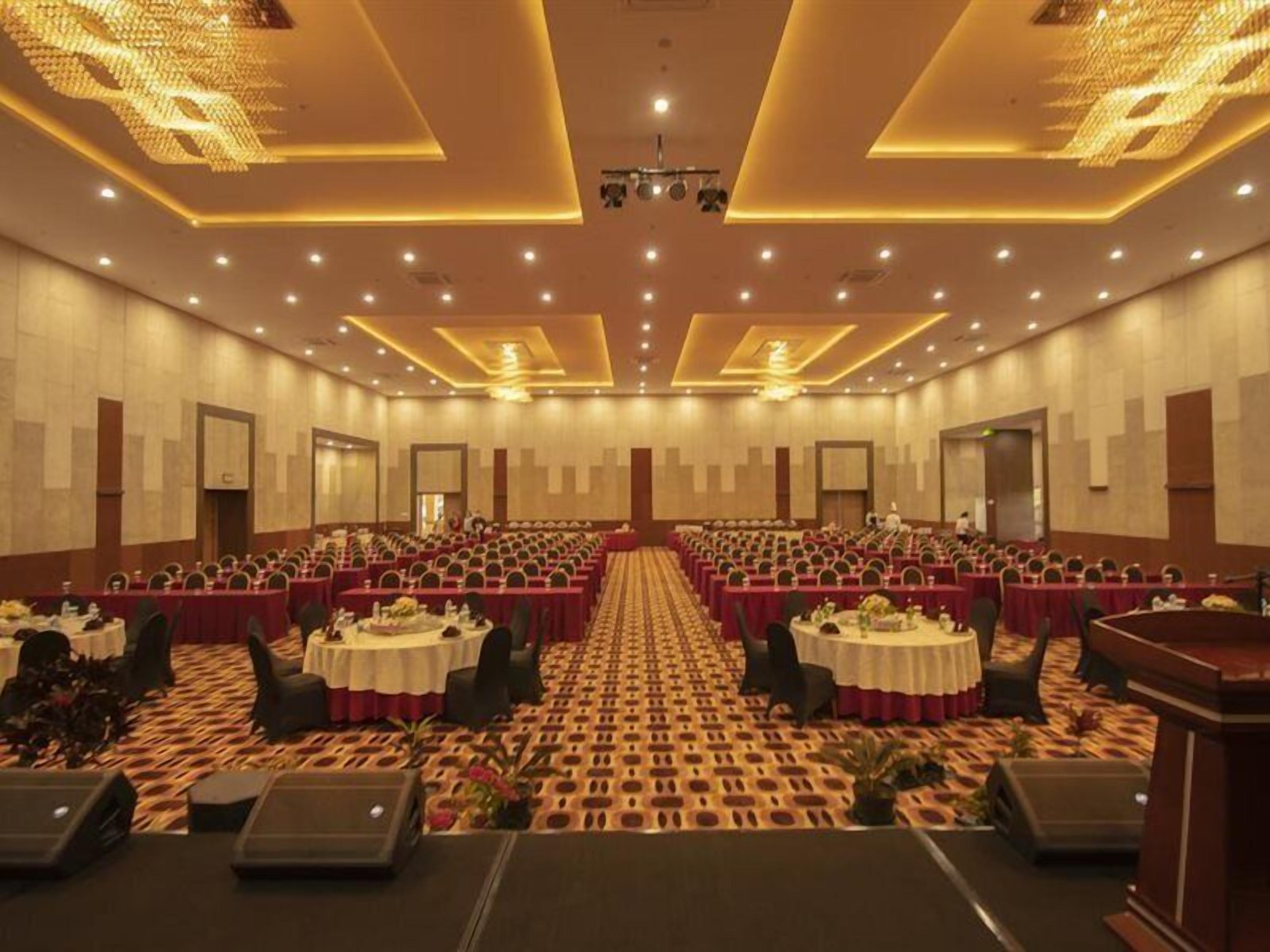 A conference room with rows of tables and chairs, a carpeted floor, and a stage at the front.