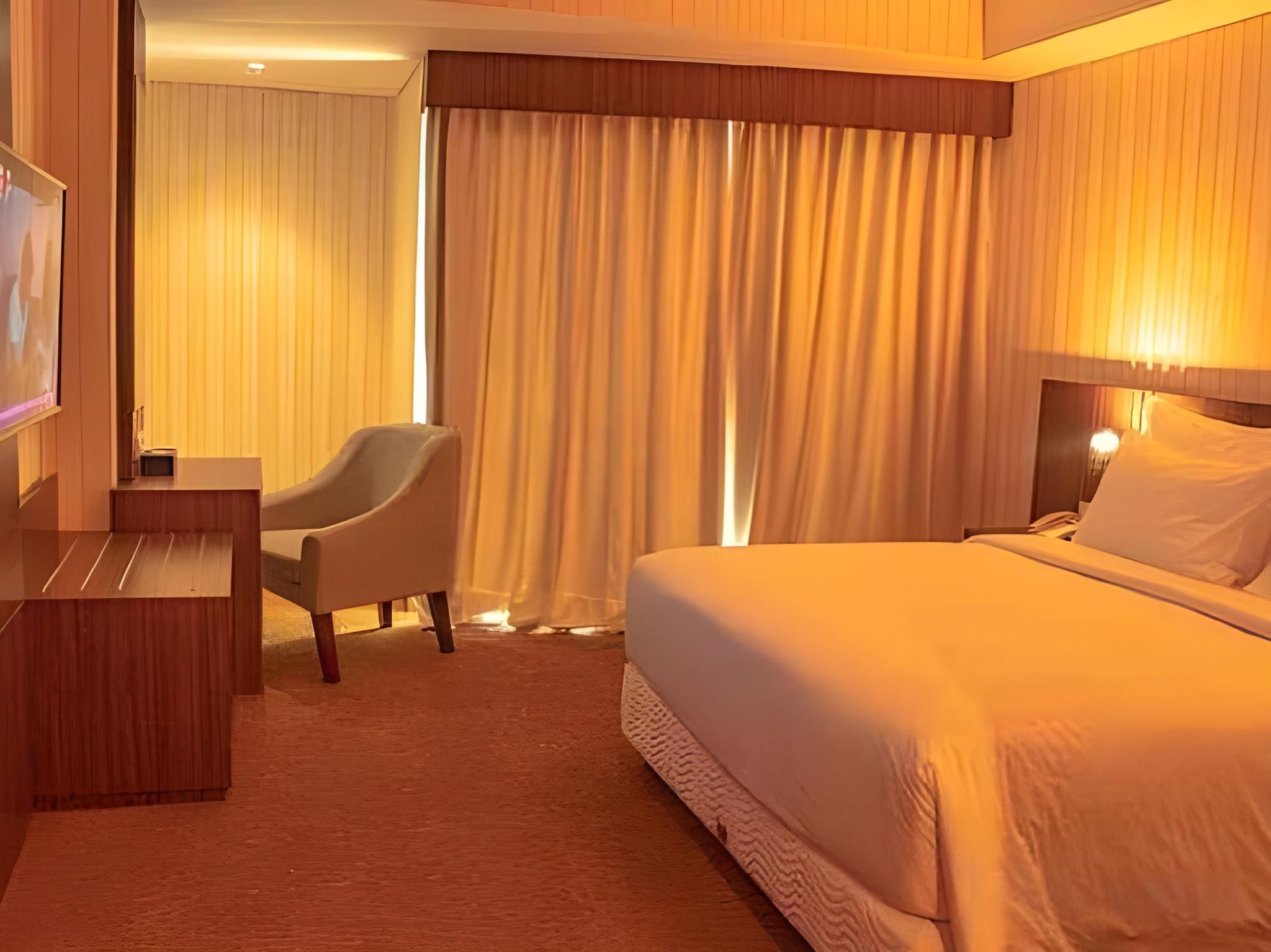 Quarto de hotel com cama, escrivaninha, cadeira e cortinas.