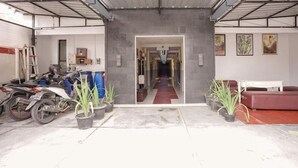 A garage with a red carpet leading to a hallway, potted plants, and a motorcycle. - Hotel O Seturan Near Hartono Mall Yogyakarta Formerly Maleo Kostel (Depok)