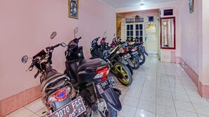 Un couloir où sont garées plusieurs motos, avec un sol carrelé et une porte au fond.