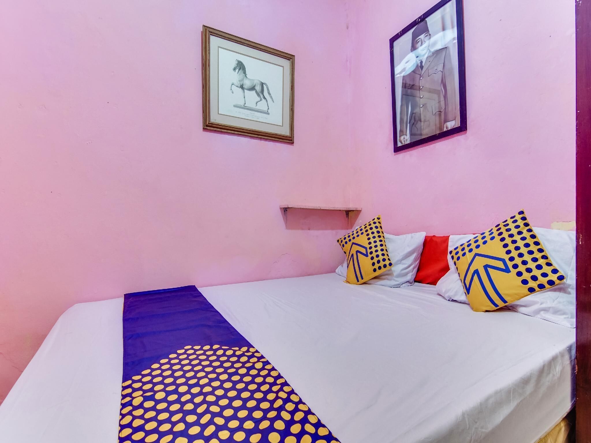 Een slaapkamer met een bed, kussens, een ingelijst beeld en een wandplank.