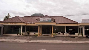Un bâtiment avec un toit recouvert de tuiles, une enseigne indiquant « Hôtel Grand Wisata », et une entrée bien visible.